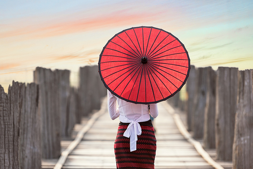 Frau mit asiatischem rotem Schirm läuft auf einem Holzweg Richtung Horizont